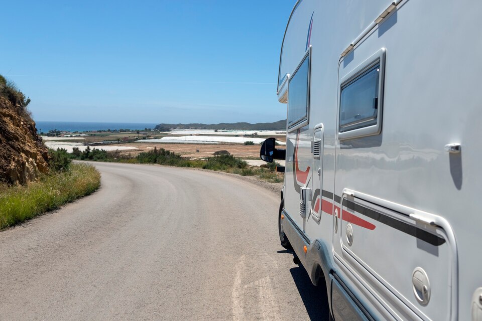 [freepicdownloader.com]-tornante-su-una-strada-secondaria-dove-c-e-un-camper-in-piedi-sul-lato-di-uno-con-vista-in-lontananza-sul-mare-e-colture-in-serra-large